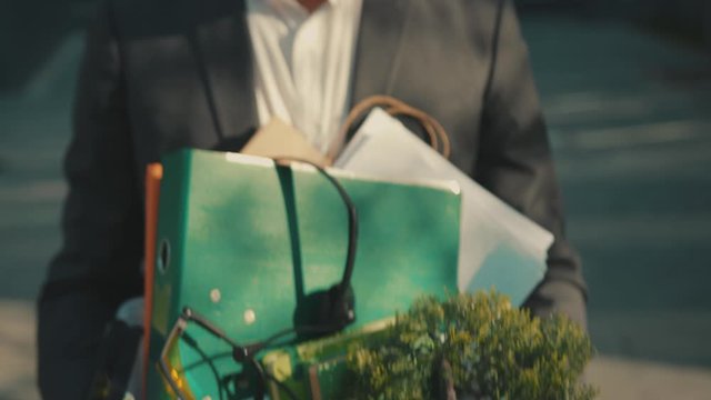 Close up sad face office worker man walking with box of personal stuff at sunlight lose a job got fired due to a coronavirus crisis unemployed business corporate employment economy slow motion