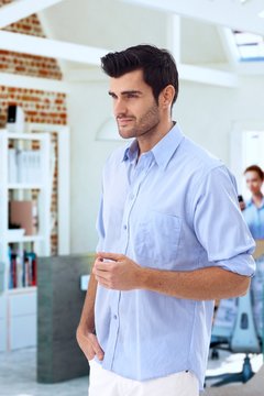Casual young man standing at office, looking away, side view.