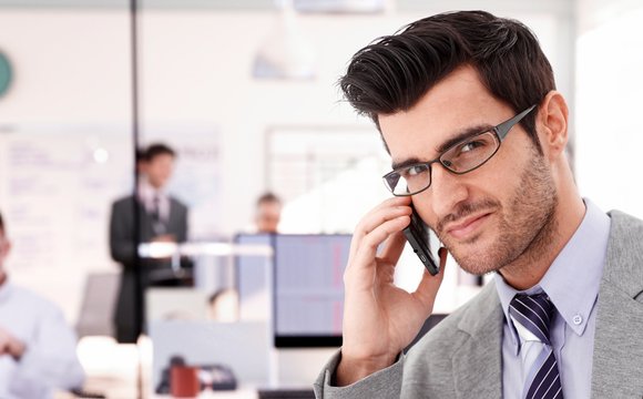 Closeup portrait of young businessman talking on mobilephone, looking at camera.