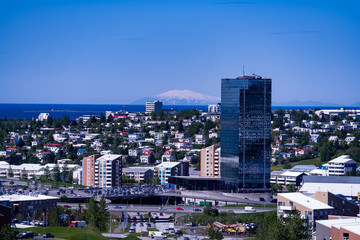 The view of Kópavogur, Iceland in the outskirts of Reykjavik.  The magnificent glacier Snæfellsjökull is seen in the distance across the water. A glass skyscraper in the foreground.