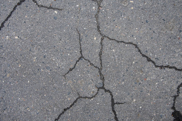 Fototapeta premium Cracked asphalt in the city, cracks and potholes on the road, textured road surface, selective focus.