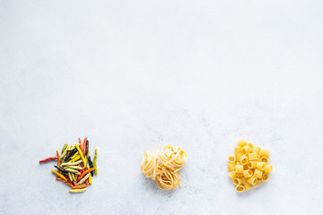 Various types of Italian pasta are on the gray table. Penne, tortellini, fusilli and Farfalle. Copy space.  Horizontal.