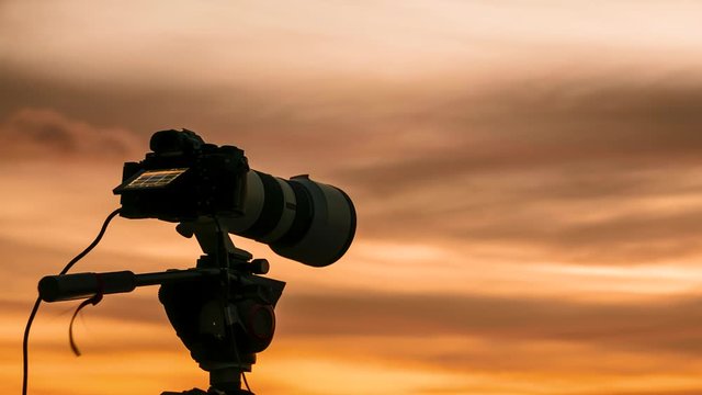 Professional camera on tripod taking picture film video of sunrise sky. Time lapse
