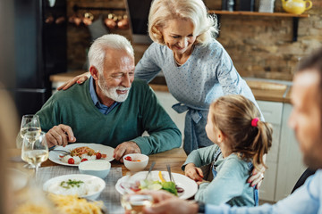 Happy grandparents talking with their granddaughter at dining table.