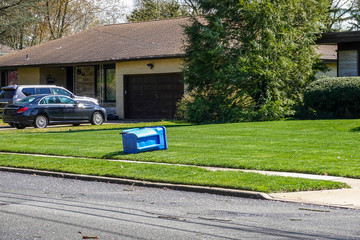 Blue recycling trash can on its side on the green lawn in front of a house