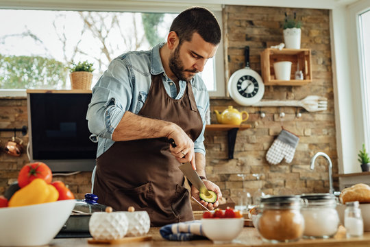Young man peeling avocado while preparing a meal in the kitchen. - Powered by Adobe