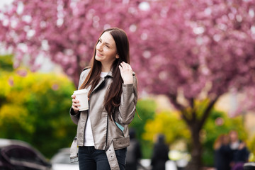 Woman in good mood posing with cup of coffee against sakura tree