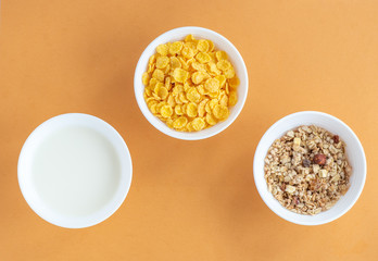 Flat lay with cornflakes, milk and muesli in three white bowls on beige background, top view. The concept of a healthy Breakfast