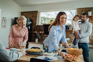 Happy woman brining food at the table while having family lunch at home.