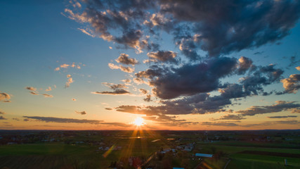 Fototapeta premium Aerial view of a Sunset over barns, silos and farmlands during the golden hour with blue sky, clouds and red sun