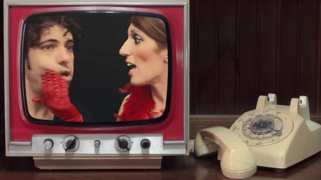A room with a rotary phone and a vintage tv showing a woman endlessly talking to a tired, sleepy man (falling down from boredom).
