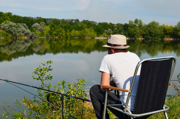  a fisherman sits on a chair and a fisherman in front of a pond fishing, Fishing on a pond on a warm day, fishing rods and feeders are thrown into the water  Fishing adventures,fisherman,