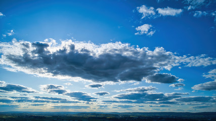Naklejka na ściany i meble Blue sky and multiple clouds background showing a horizon and a hidden sun
