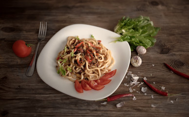 spaghetti with vegetables on a white plate. Textured wooden table. Bitter peppers and tomatoes