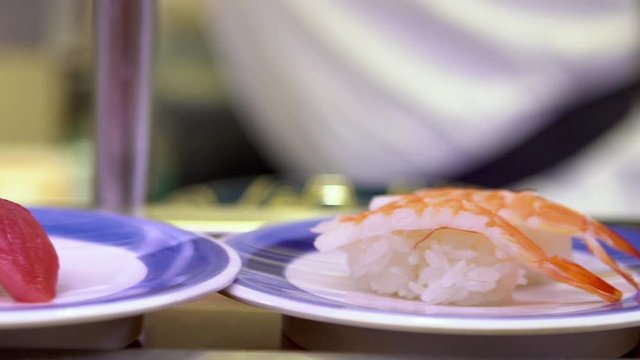 Slow motion of sushi on moving conveyor belt in a Japan restaurant. Traditional Kaitenzushi Japanese food. Shushi Go Round is a famous form of fast food common in Asia, also known as sushi train.-Dan