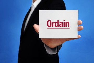 Ordain. Lawyer in a suit holds card at the camera. The term Ordain is in the sign. Concept for law, justice, judgement