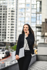 A young woman in smart casual wear with a laptop is walking on the cases, she is talking on the smartphone