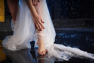 Beautiful female feet in the water with splashes. Photo in a neon light in the studio. White veil or long dress