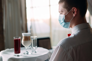 A European-looking waiter in a medical mask serves Latte coffee.