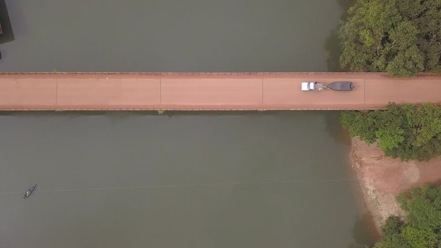 Drone aerial view of pickup truck driving on dirt road bridge over Teles Pires river towing fishing motorboat on trailer in Amazon, Mato Grosso, Brazil. Concept of travel, transport and leisure. 4K