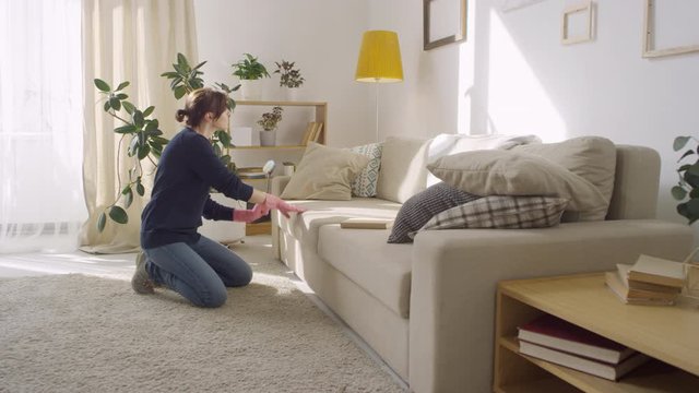 Slowmo of happy young woman in pink latex gloves having fun and drumming beat on couch while listening to music and cleaning flat