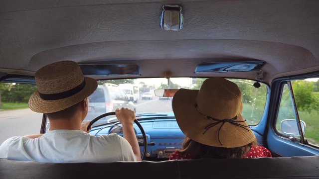 Young couple in hats riding at vintage car during road trip. Unrecognizable man and woman sitting at the front seat of old retro car. Travel concept. Slow motion Rear back view Close up