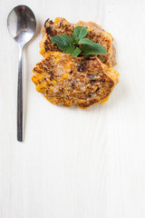 Vegan breakfast pancakes, peppermint and teaspoon on white wooden background. Metal spoon with two fritters on right and green leaves above. Vertical picture, main object on top  , copy space below 