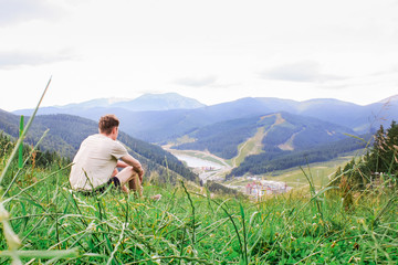 One guy enjoying view of nature in the ukrainian mountains. Young man sits on the mountain hilltop on a green grass. Hiker man climbed on the mountain top. Scenic view to carpathian mountains, Ukraine