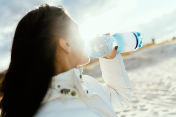 Women holding and drinking large plastic water bottle with a seascape background