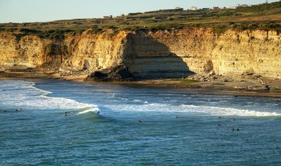 surfers riding waves below scenic cliffs in Riberira d'Ilhas