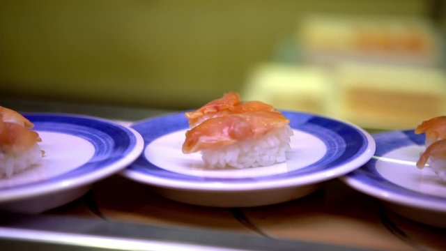 4K, Sushi on moving conveyor belt in a Japan restaurant. Traditional Kaitenzushi Japanese food. Shushi Go Round is a famous form of fast food common in Asia, also known as sushi train.-Dan