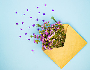 Purple field spring flowers in an envelope and small glittering stars on a pastel blue background. background for greeting women's days and Valentine's day