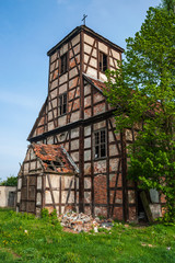 Fototapeta na wymiar Ruins of the abandoned evangelical timber framing church made as half-timbered house with wood and red bricks. Blue sky and green grass and tree.