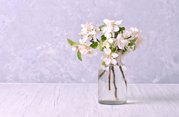 Spring branches of a blossoming apple tree in a glass jar on wooden table