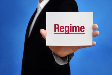 Regime. Lawyer in a suit holds card at the camera. The term Regime is in the sign. Concept for law,...