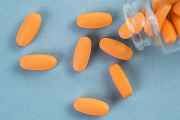 Orange pills pouring out of the glass jar on blue background