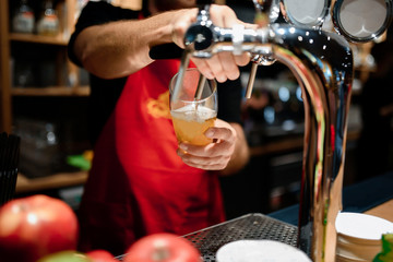 Barman hands pouring a lager cider in a glass.