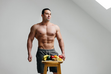 Sexy vegan guy with a naked torso posing in the Studio next to fruit. Diet. Healthy diet