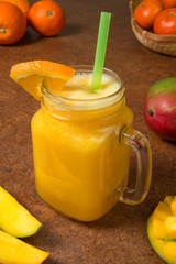Mango orange and tangerine smoothie with ingredients on a brown background. Selected focus.