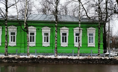 Beautiful old wooden green house on the street behind the birches in winter with big white windows.Totma.Vologda region.Russia.