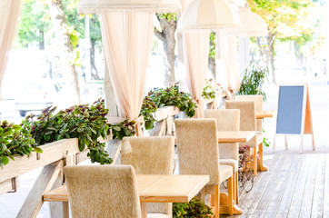 Outdoor cafe, terrace. Chairs and wooden tables on the terrace with beautiful greens in a cozy cafe
