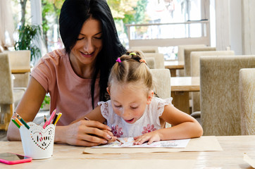 A happy family. Mother and daughter smiling together with colored pencils at the table