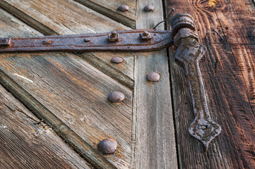 Close-up of an old, corroded and rusty hinge holding the wooden door. Details of wood and metal structure and soft focus.