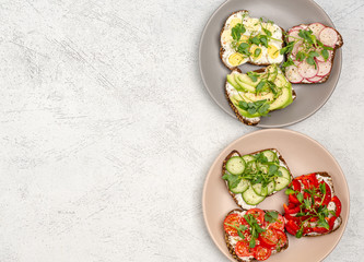 A variety of mini sandwiches with cream cheese and vegetables on plates on a light background.