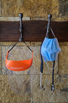 face mask or surgical chinstrap, an stethoscope and a plastic face protector hanging