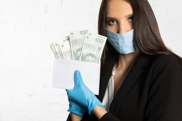 Businesswoman in a protective mask and protective gloves puts a bundle of paper banknotes into the envelope.