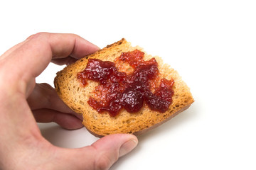 Closeup of strawberry jam on cracker slice in hand on white background