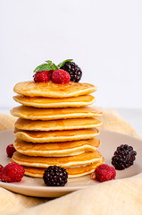 Homemade classic American pancakes with fresh raspberries, blackberries, honey and mint leaves, on a light background.