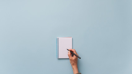 Top view of female hand writing in blank notepad