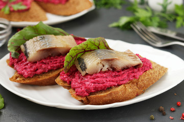 Beet, cream cheese and herring sandwiches on white plate on dark concrete background, Closeup